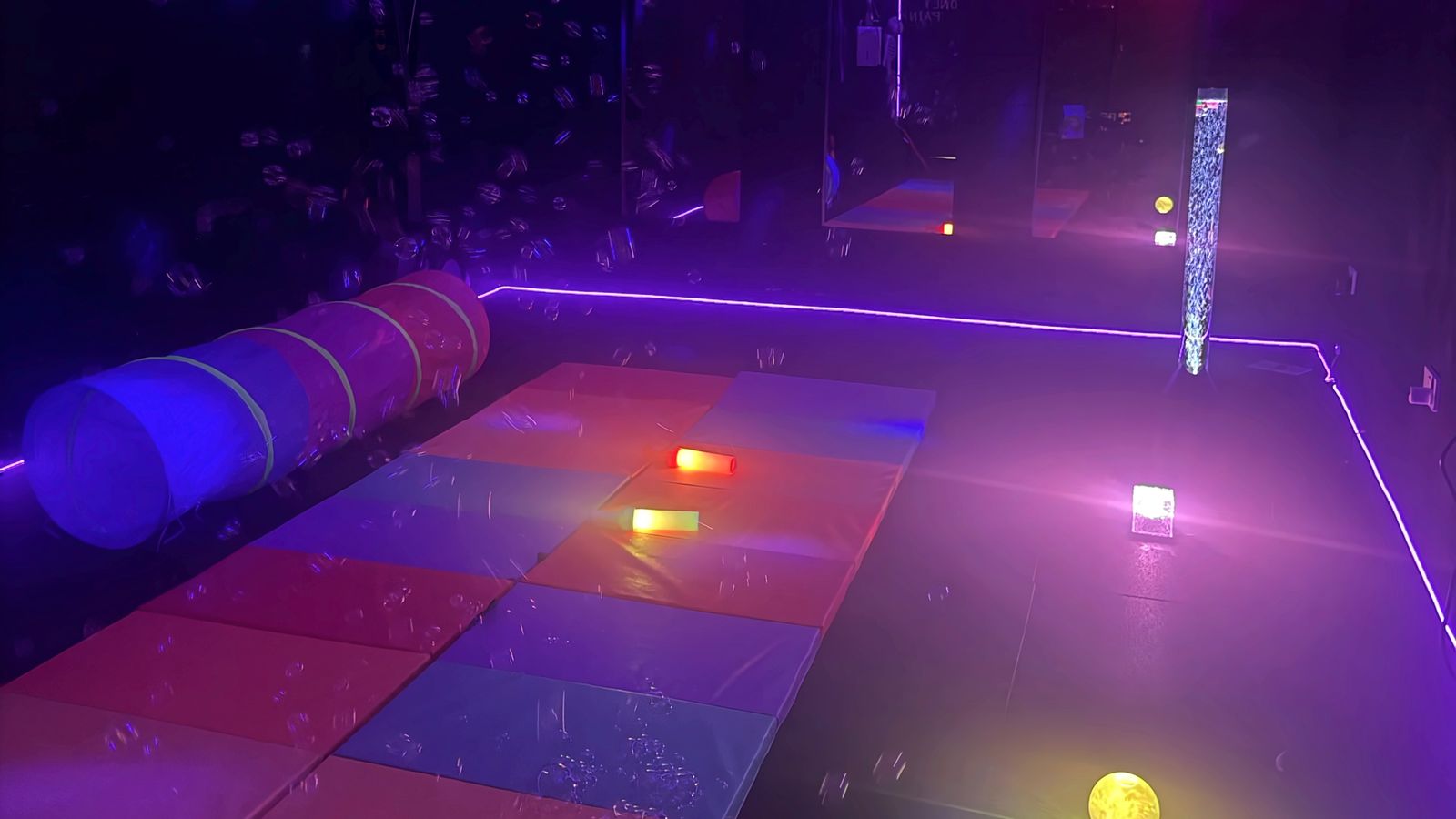 The ElectroSensory sensory room in New Ash Green, glowing purple, with colourful soft mats, a play tunnel, a bubble tube and floating bubbles